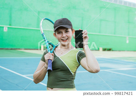 female tennis player holding racket while showing phone screen 99817421