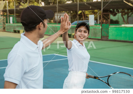 Mixed doubles tennis athletes high-five each other celebrating victory 99817530