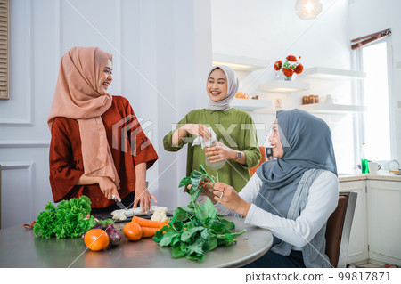 woman wearing hijab with best friend preparing food for dinner 99817871