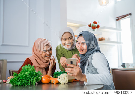 friend with hijab looking at the phone to make food 99818099