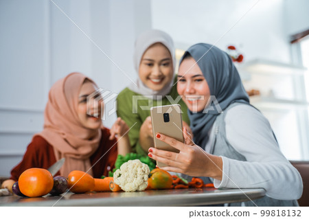 friend with hijab looking at the phone to make food friend with hijab looking at the phone to make food 99818132