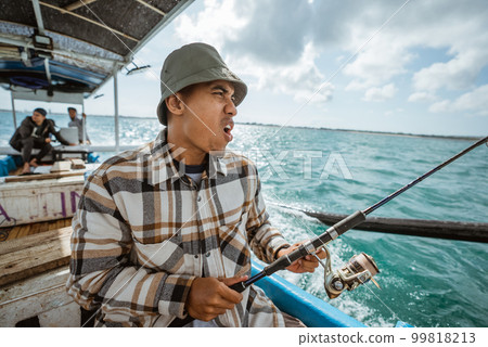 Asian fisherman excited while fishing on small boat at sea Asian fisherman excited while fishing on small boat at sea 99818213
