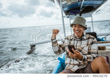 excited angler using cell phone while resting on fishing boat excited angler using cell phone while resting on fishing boat 99818270