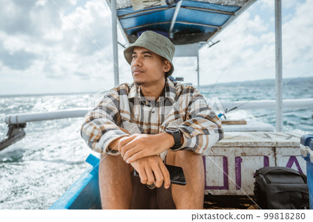 angler sits holding a cell phone on a fishing boat 99818280