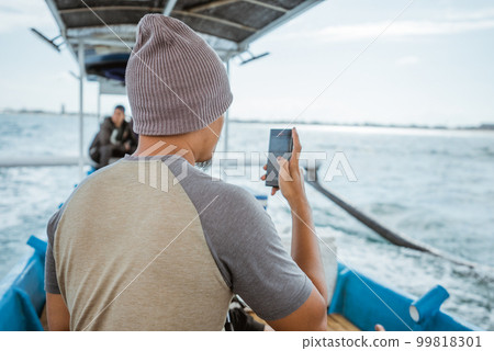 seen from behind fisherman using cellphone on small fishing boat 99818301