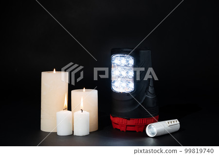 Electric flashlights and burning candles on a black background, alternative sources of light and heat Electric flashlights and burning candles on a black background, alternative sources of light and heat 99819740