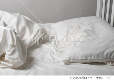 Unmade bed, satin white linen, white bed, pillow and blanket 99819848