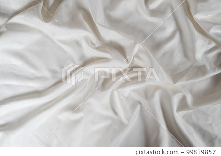 Satin crumpled fabric of light milky color, top view. Natural bed linen, sheets, abstract background of luxury fabric, wavy folds 99819857