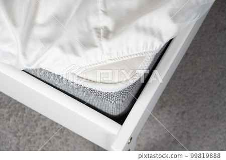 White satin sheet on an elastic band on the mattress. Bed linen on the bed White satin sheet on an elastic band on the mattress. Bed linen on the bed 99819888