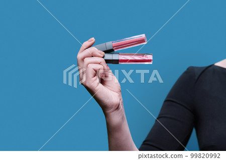 Close-up of two trendy lip glosses in hand, on blue background Close-up of two trendy lip glosses in hand, on blue background 99820992