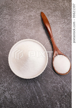 Organic sweetener Erythritol, produced by fermentation from corn, called dextrose in ceramic bowl, wooden spoon on granite background, table. Sugar substitute. Vertical plane, top view 99821397