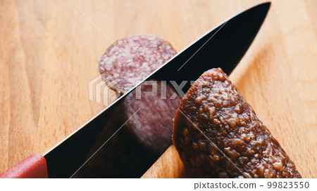 Sharp kitchen knife cuts salami close up Sharp kitchen knife cuts salami close up 99823550