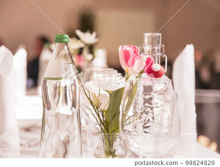Festive decorated table in a restaurant, wine glasses, vase, flowers, mineral water bottles, textiles, cutlery on a white tablecloth. Restaurant, celebration, wedding 99824820