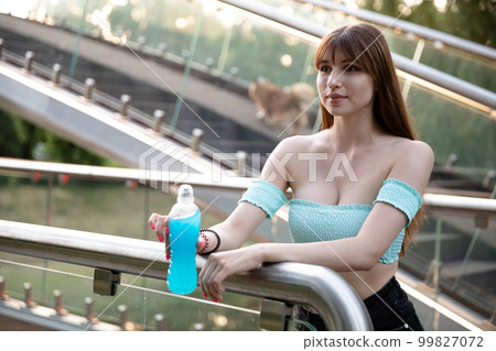 A long-haired brunette with bangs stands by a glass railing. A long-haired brunette with bangs stands by a glass railing. 99827072