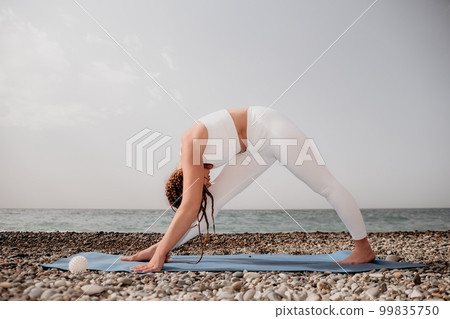 Woman sea yoga. Well looking middle aged woman with braids dreadlocks in white leggings and tops doing stretching pilates on yoga mat near sea. Female fitness yoga routine concept. Healthy lifestyle. 99835750