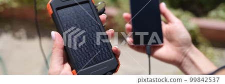 Female hand holding solar power bank and mobile phone closeup 99842537