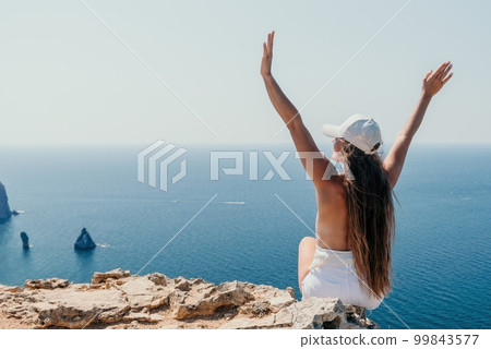 Woman summer travel sea. Happy tourist enjoy taking picture outdoors for memories. Woman traveler posing over sea bay surrounded by volcanic mountains, sharing travel adventure journey 99843577