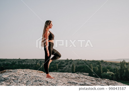 Fitness woman. Well looking middle aged woman with long hair, fitness instructor in leggings and tops doing stretching and pilates on the rock near forest. Female fitness yoga routine concept. 99843587
