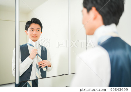 A young office worker man tightening his tie in front of the mirror A young office worker man tightening his tie in front of the mirror 99843699