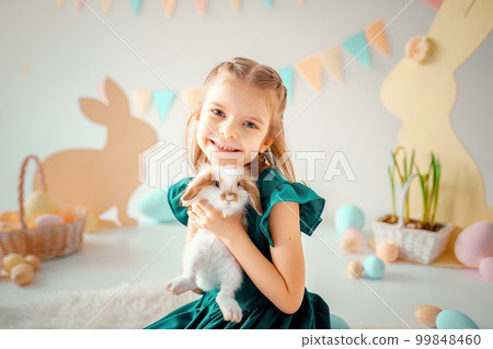 Happy little girl holds fluffy rabbit on Easter colorful decor background. Easter concept  99848460