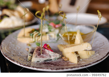Four types of different cheeses sliced and served on a plate with honey sauce. 99849762