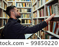 Student choosing books in library according to list on tablet 99850220