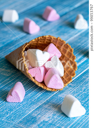 Waffle cone with heart-shaped marshmallows, close-up on a blue wooden background. Waffle cone with heart-shaped marshmallows, close-up on a blue wooden background. 99853767