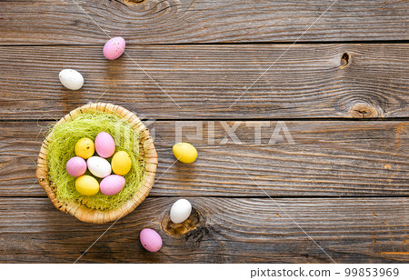 Easter eggs in a decorative nest on a wooden background, top view. Easter eggs in a decorative nest on a wooden background, top view. 99853969