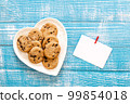 Plate with cookies and a piece of paper on a wooden background, flat lay. 99854018
