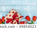 Red tulips and a gift box on a blue wooden background, top view. 99854023