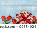 Red tulips and a gift box on a blue wooden background, top view. 99854024