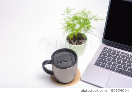 A desk with a computer, a mug, and a houseplant 99854064