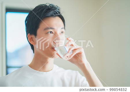 A young man drinking a glass of water to hydrate A young man drinking a glass of water to hydrate 99854832