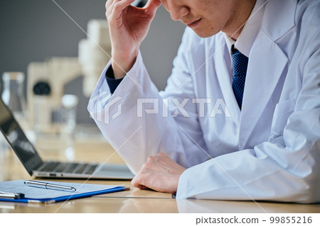 A man in a white coat who fails at work and holds his head 99855216