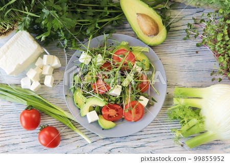 Salad of microgreens, avocado, tomatoes, cheese and arugula, on a plate, against the background of fennel and greens, recipe from natural ingredients, healthy food  99855952
