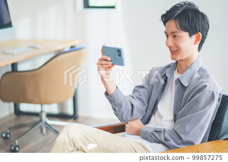 年輕人坐在沙發上，在智能手機上觀看視頻 99857275