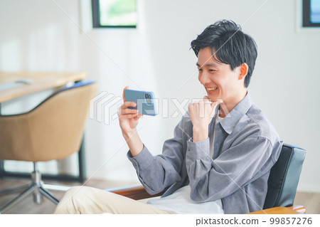 年輕人坐在沙發上，在智能手機上觀看視頻 99857276