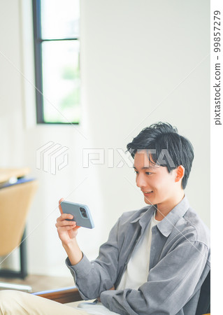 Young man sitting on sofa and watching videos on smartphone Young man sitting on sofa and watching videos on smartphone 99857279