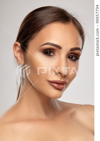 Close up portrait of a brunette nude model girl with professional evening make-up and plump lips, posing on gray background. 99857794
