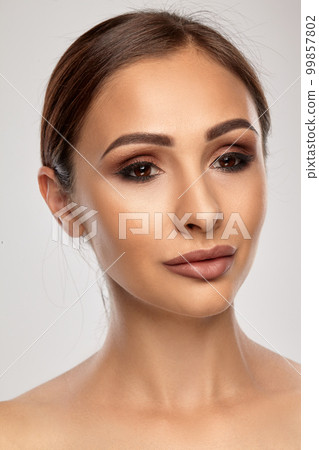 Close up portrait of a brunette nude model girl with professional evening make-up and plump lips, posing on gray background. 99857802