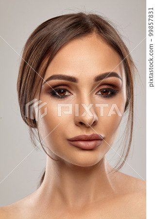 Close up portrait of a brunette nude model girl with professional evening make-up and plump lips, posing on gray background. Close up portrait of a brunette nude model girl with professional evening make-up and plump lips, posing on gray background. 99857831