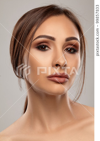 Close up portrait of a brunette nude model girl with professional evening make-up and plump lips, posing on gray background. Close up portrait of a brunette nude model girl with professional evening make-up and plump lips, posing on gray background. 99857833