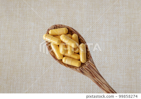 Coenzyme Q10 vitamin capsules in a wooden spoon on a beige background. Top view, copy space. Close-up. 99858274