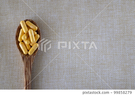 Vitamin Coenzyme Q10 capsules in a wooden spoon on a beige background. Top view, copy space. 99858279