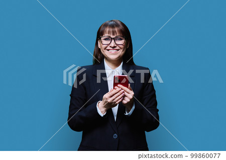 Smiling middle aged business woman using smartphone, blue background Smiling middle aged business woman using smartphone, blue background 99860077