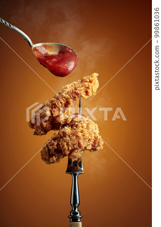 Fried chicken with ketchup on a fork. 99861036