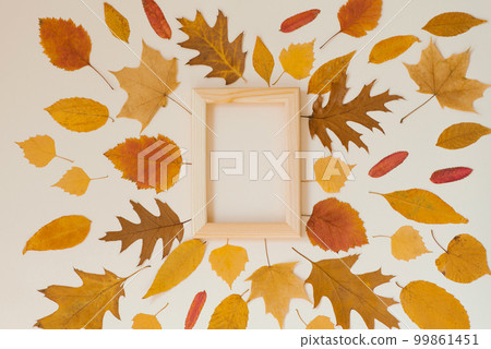 An empty wooden frame surrounded by yellow fallen leaves on a beige background. Autumn fla lay 99861451