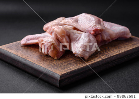 Raw chicken wings with salt, spices and herbs on a wooden cutting board Raw chicken wings with salt, spices and herbs on a wooden cutting board 99862691