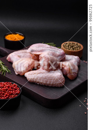 Raw chicken wings with salt, spices and herbs on a wooden cutting board Raw chicken wings with salt, spices and herbs on a wooden cutting board 99862725