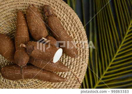Organic raw cassava tuber on wicker tray and palm leaves. 99863383